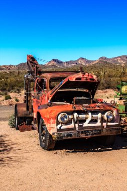 Eski kırmızı bir kamyon çölde park halinde. Kamyon paslanmış ve kırık bir penceresi var. Olay yeri ıssız ve ıssız, etrafta başka araç ya da insan yok.