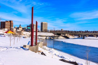 Üzerinden bir nehir akan ve üzerinde bir köprü olan bir şehir. Gökyüzü açık ve mavi