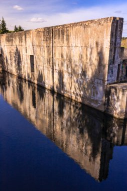 Önünde bir su kütlesi olan büyük bir duvar. Su duvarı ve gökyüzünü yansıtıyor.