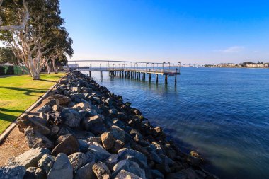 Rıhtımı ve iskelesi olan kayalık bir kıyı şeridi. Su sakin ve gökyüzü berrak.