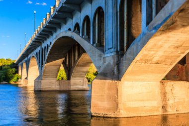 Altında nehir akan bir köprü. Köprü betondan yapılmıştır ve çok fazla kemeri vardır. Su sakin ve gökyüzü mavi.