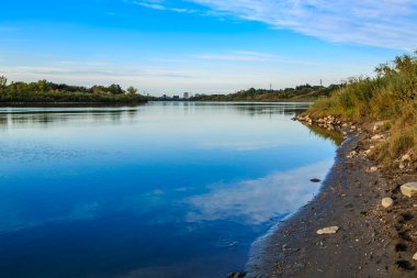 Arka planda mavi gökyüzü olan sakin bir su kütlesi. Su durgun ve gökyüzü berrak.