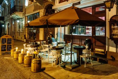 Dışarıda büyük bir şemsiyesi ve birkaç sandalyesi olan bir restoran. Sandalyeler boş ve şemsiye açık.