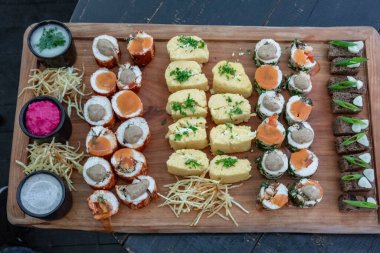 A wooden tray with a variety of sushi rolls and other food items. The tray is set up for a party or gathering