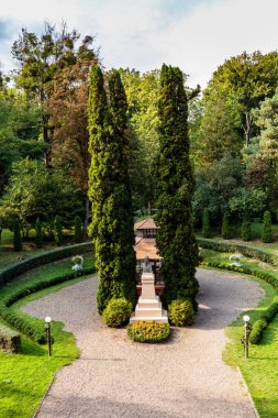 Taştan geçitli bir patika ve ortasında küçük bir taş yapı. Yol ağaçlar ve çalılarla çevrili.