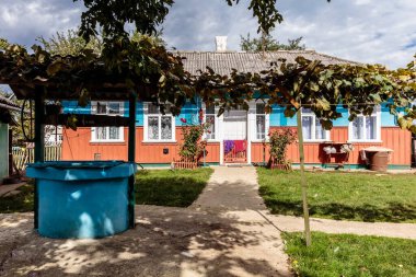 Önünde kuyu olan mavi bir ev. Ev bir sürü bitkiyle çevrili bir bahçeyle çevrili.