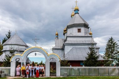 Bir grup insan altın çatılı büyük beyaz bir binanın önünde duruyor. Bina bir kilise gibi görünüyor ve insanlar turist ya da ziyaretçi gibi görünüyor. Sahne bir merak konusudur.