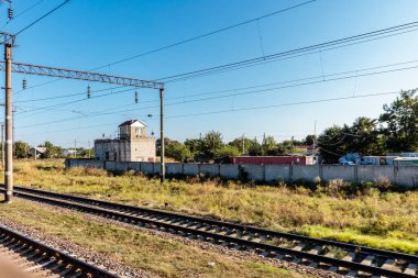 Bir tren raylarda ilerliyor, üzerinde gökyüzü açık ve mavi görünüyor. Tren sabit bir hızda hareket ediyor, ve çevredeki alan çoğunlukla boş, sadece birkaç ağaçla.