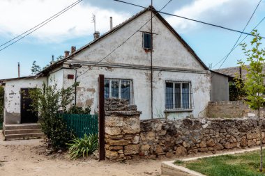 Taş duvarı ve yeşil çiti olan küçük bir ev. Ev eski ve çok paslı.
