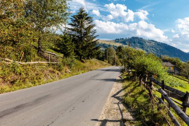 Yan tarafında çit, arka tarafında ağaçlar olan bir yol. Yol boş ve gökyüzü mavi.