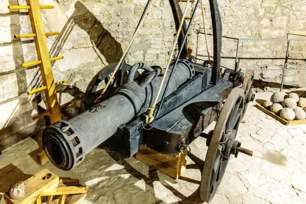 Bir top merdiveni ve kaya yığınıyla dolu bir odada oturuyor. Top eski ve paslı, ve tarihi bir eser gibi görünüyor. Sahne biraz ürkütücü ve gizemli.