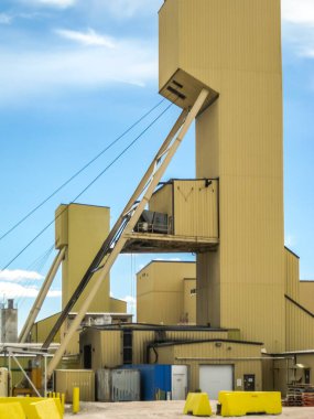 Üzerinde bir sürü makine ve vinç olan büyük sarı bir bina. Bina sarı bir bariyerle çevrili.