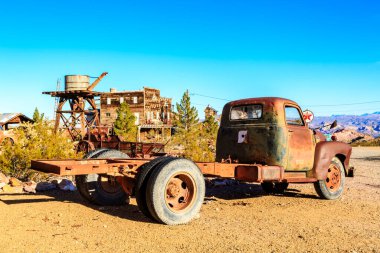 Eski bir kamyon çölde park halinde. Kamyon paslanmış ve yatağı var. Çöl çorak ve kuru.