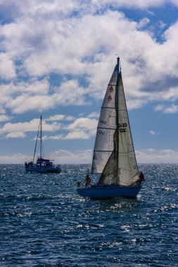 Arka planda bulutlu bir gökyüzü olan bir yelkenli okyanusta gidiyor. Görünürde sadece yelkenli var.