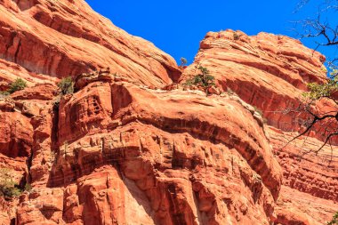 Arka planda mavi gökyüzü olan kayalık bir dağ. Dağ kırmızı kayalarla kaplı ve benzersiz bir şekli var.
