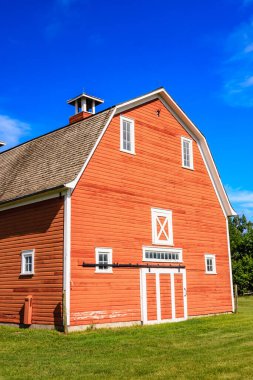Beyaz çatılı ve beyaz kapılı kırmızı bir ahır. Ahır yeşil bir tarla ile çevrili.