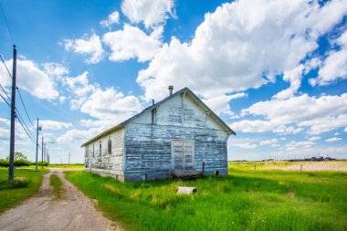 Verandası ve bacası olan küçük, eski, beyaz bir bina. Bina bir çimen tarlası ile çevrilidir.