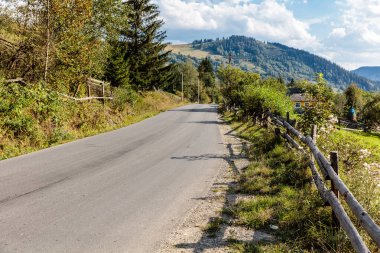 Yan tarafında çit, arka tarafında ağaçlar olan bir yol. Yol boş ve üzerinde kimse yok.