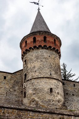 Sivri çatılı uzun tuğla bir kule. Kule kırmızı tuğlalarla kaplı ve tepesinde rüzgar gülü var. Gökyüzü bulutlu ve kule görüntüdeki tek görünür nesne.