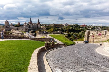 Bir grup asker bir kalenin önündeki kaldırım taşı caddesinde yürüyor. Gökyüzü bulutlu ve atmosfer huzurlu.