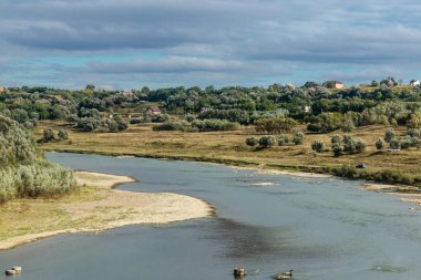 Arka planda bir sürü ağaç ve ev olan bir nehir. Su sakin ve berrak.