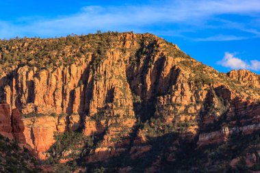 Kayalık bir arazisi ve mavi gökyüzü olan bir dağ. Dağ ağaçlar ve kayalarla kaplı.