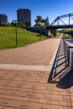 Sağ tarafında çit olan bir tuğla geçit. Geçit bir nehrin yanında ve üzerinde bir köprü var.