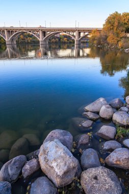 Bir köprü sakin mavi bir suyla bir nehri kaplar. Köprü kayalar ve ağaçlarla çevrili.