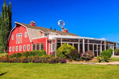 Üstünde yel değirmeni olan kırmızı bir ahır ve cam çatılı beyaz bir bina. Ahır yemyeşil bir çimenlik ve çiçekli bir bahçeyle çevrilidir. Sahne huzurlu ve davetkâr, ahırla birlikte.