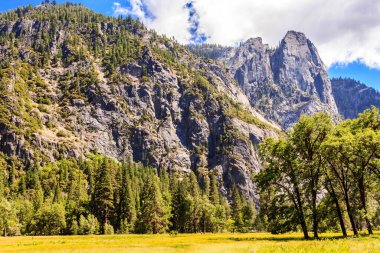 Önünde büyük bir tepe olan bir dağ sırası. Tepe ağaçlarla kaplı ve gökyüzü açık.