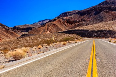 Ortasında sarı çizgi olan bir yol. Yol boş ve gökyüzü mavi.
