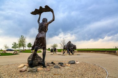 Elinde büyük bir kaya tutan bir kadın heykeli. Heykel kayalarla çevrili ve bir parkta bulunuyor.