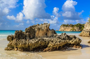 Sahilde büyük bir kaya var, arkasında da okyanus var. Kaya kumla çevrili ve gökyüzü bulutlu. Sahne huzurlu ve huzurlu, kaya bir istikrar hissi veriyor.
