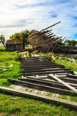 Yanı başında büyük bir odun yığını olan harap olmuş eski bir bina. Bina bir ahır gibi görünüyor ve ahşap da çatıdan. Olay yeri ıssız ve terk edilmiş.