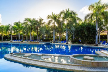 Etrafında bir sürü ağaç olan bir havuz. Havuz mavi ve etrafında bir sürü sandalye var.