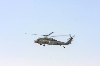 Bir askeri helikopter gökyüzünde uçuyor. Gökyüzü açık ve mavi. Helikopter havada ve o hareket halinde.