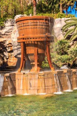 İçinden su akan büyük, kırsal bir fıçı. Fıçı taştan bir duvar ve yemyeşil bir çalıyla çevrili.