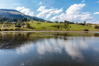 Gökyüzünün yansıması ve arka planda dağların olduğu sakin bir göl. Huzurlu ve huzurlu bir sahne.