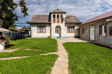 Bahçesinde beyaz çitleri ve küçük beyaz kulübesi olan büyük bir ev. Ev yemyeşil bir çimenlikle çevrili.