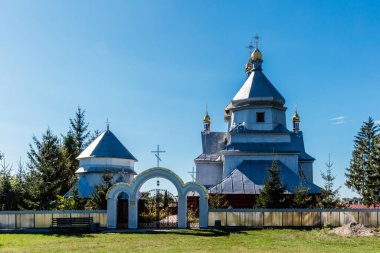 Beyaz çatılı ve arkasında mavi gökyüzü olan büyük bir kilise. Kilise ağaçlar ve çitlerle çevrili.