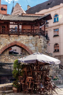 Küçük bir grup sandalye büyük bir şemsiye altında üst üste istiflenir. Sandalyeler eski ve paslı ve şemsiye de siyah. Sahne nostalji hissi veriyor.