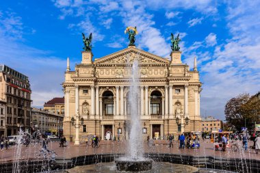 A large building with a fountain in front of it. The fountain is spraying water into the air. There are many people walking around the fountain and the building. The scene is lively