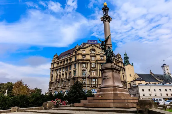 Üstünde bir adamın heykeli olan yüksek bir bina. Binanın etrafı fıskiyeli ve saksı bitkileriyle çevrili.