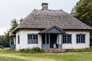 Sazlı çatısı ve mavi panjurları olan küçük bir ev. Ev yemyeşil bir çimenlikle çevrili.