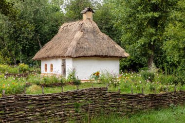 Sazdan çatılı küçük beyaz bir ev bir çiçek tarlasında oturur. Ev ahşap bir çit ve küçük bir bahçe ile çevrilidir. Huzurlu ve huzurlu bir sahne.