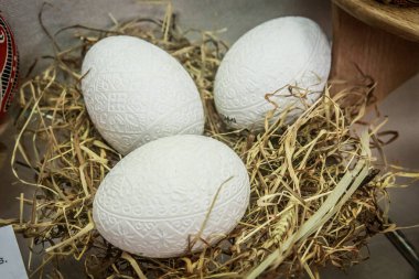 Üç beyaz yumurta samandan yapılmış bir yuvada duruyor. Yumurtalar karmaşık tasarımlarla süslenir ve yuva kurumuş ottan yapılır. Sıcaklık ve rahatlık kavramı