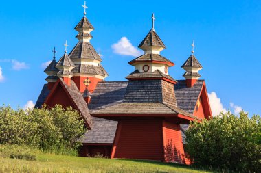 Arka planda mavi gökyüzü olan kırmızı bir kilise. Kilise ağaçlarla çevrili ve huzurlu bir atmosferi var.