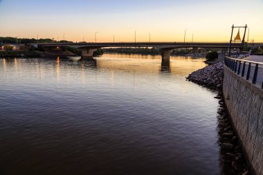 Bir köprü gün batımında bir nehri kapsar. Su sakin ve gökyüzü güzel turuncu bir renktir.