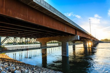 Bir köprü aşağıdaki su manzaralı bir nehri kapsar. Köprü betondan yapılmıştır ve kırsal bir görünüme sahiptir.