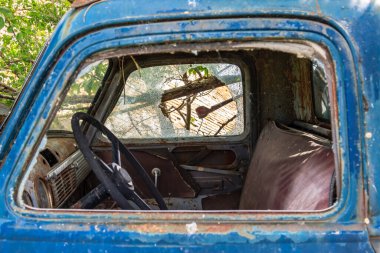 Kırık ön camı ve deri koltuğu olan mavi bir kamyonet. Koltuk parçalanmış ve kamyon da eski.